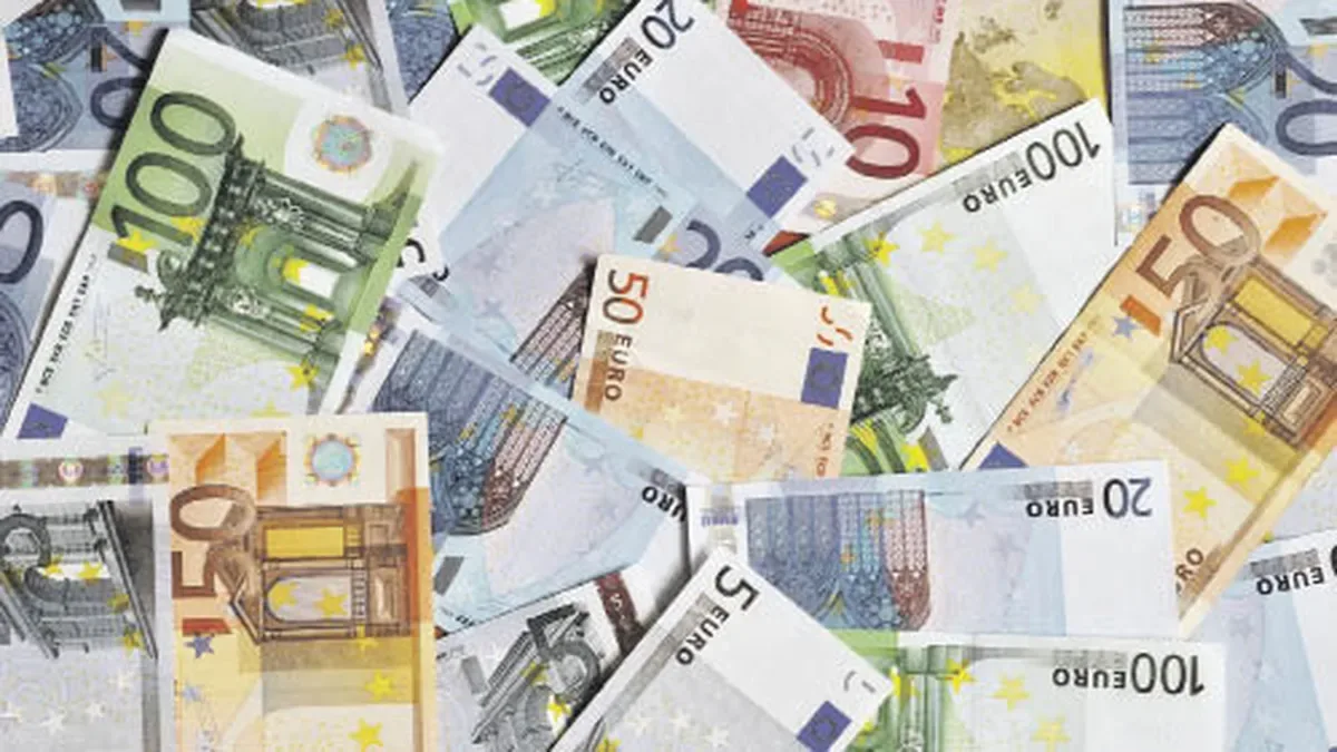 Billetes de euros y pesos argentinos sobre una mesa con cotizaciones en pantalla